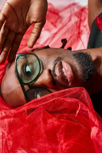 Portrait of handsome african american man with red tulle fabric lying on floor, fashion concept — Stock Photo