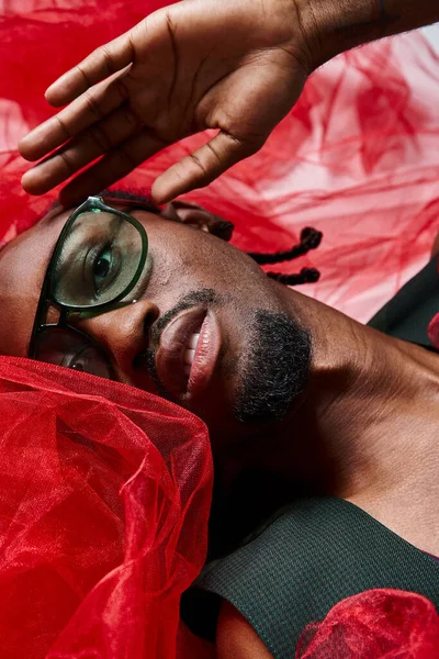 Portrait of appealing african american man with red tulle fabric lying on floor, fashion concept — Stock Photo