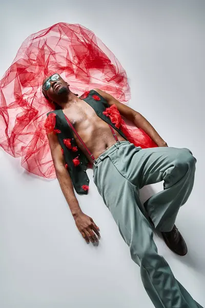 Verführerische junge afrikanisch-amerikanische männliche Modell in lebendiger Kleidung mit rotem Tüll auf dem Boden liegend — Stockfoto