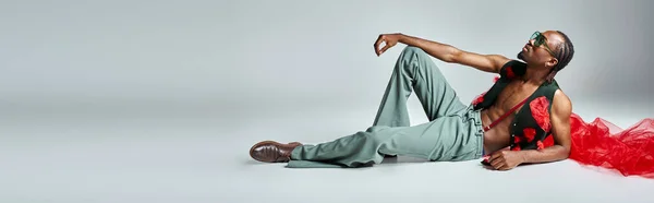Handsome african american man in stylish attire with red tulle fabric reclining on floor, banner — Stock Photo