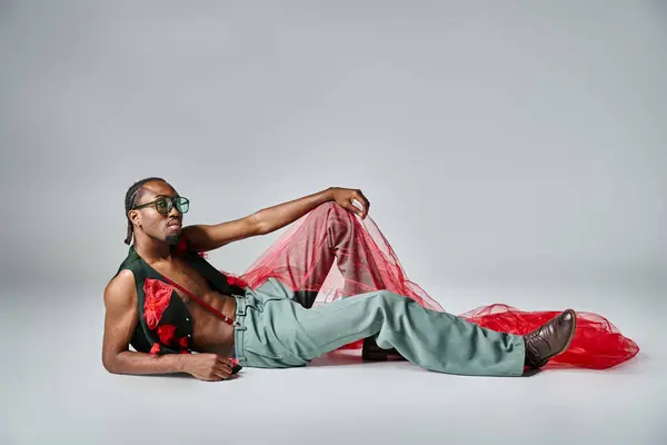 Charming african american man in fashionable attire with red tulle fabric reclining on floor — Stock Photo