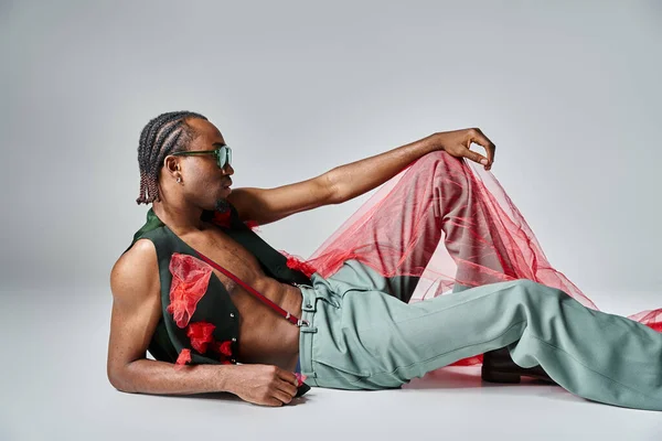 Appealing african american man in fashionable attire with red tulle fabric reclining on floor — Stock Photo