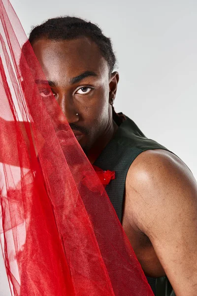 Schöne junge afrikanisch-amerikanische männliche Modell posiert mit lebendigem roten Tüll Stoff auf grauem Hintergrund — Stockfoto