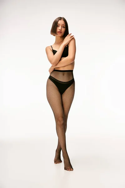 Bastante joven asiático modelo en negro ropa interior y medias de rejilla posando sobre fondo blanco - foto de stock