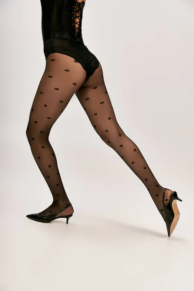 Cropped shot of chic woman in corset, polka dot tights and high heels walking on white backdrop — Stock Photo