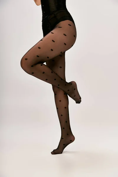 Corte tiro de mulher chique em espartilho preto e meia polka dot posando no fundo branco, dedo do pé ponta — Fotografia de Stock