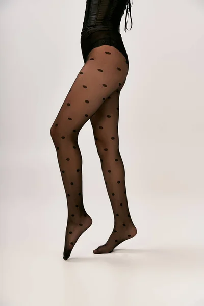 Обрезанное фото шикарной женщины в черном корсете и трико в горошек позирует на белом фоне, пальчик на ноге — стоковое фото