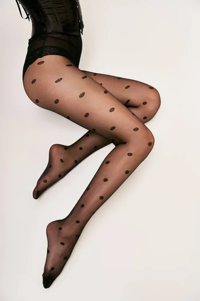 Foto recortada de modelo glamouroso em espartilho preto e meias de bolinhas deitado no chão branco — Fotografia de Stock