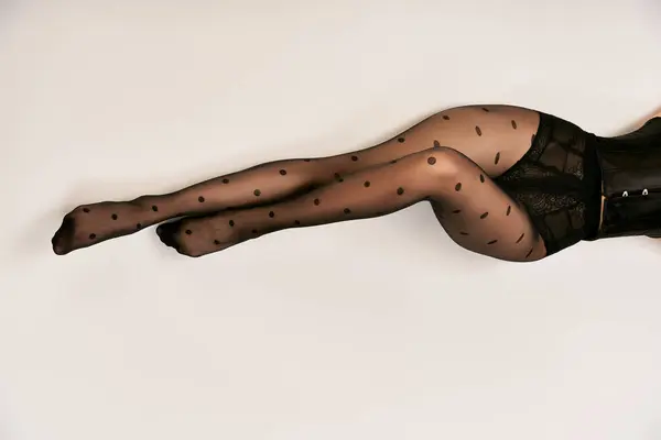 Vista superior de mujer joven recortada en corsé negro y medias de lunares tumbadas en el suelo blanco - foto de stock