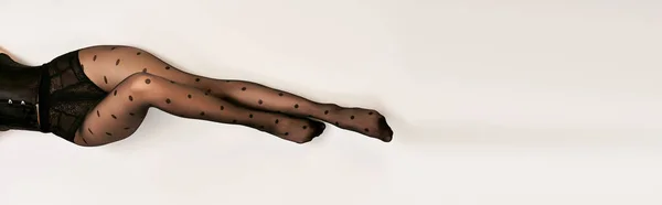 Vista superior da mulher jovem cortada em espartilho preto e meia-calça bolinha deitada no chão branco, banner — Fotografia de Stock