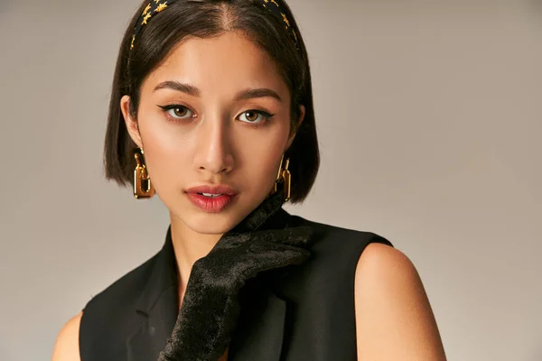 Красива азіатська жінка в елегантному вбранні дивиться на камеру і позує на сірому фоні, рука в рукавичці — стокове фото