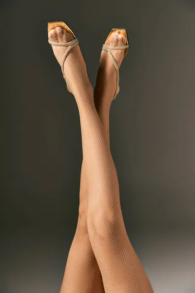 Eleganti calze a rete su donna con gambe incrociate in posa in calzature dorate su fondo grigio — Foto stock