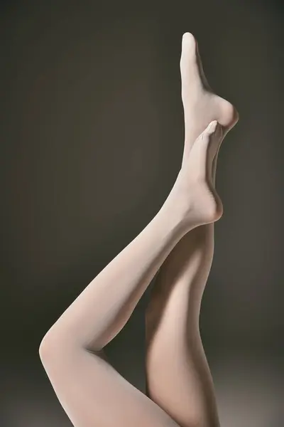 Vue recadrée du jeune modèle en collants blancs transparents posant avec les jambes levées sur fond gris foncé — Photo de stock