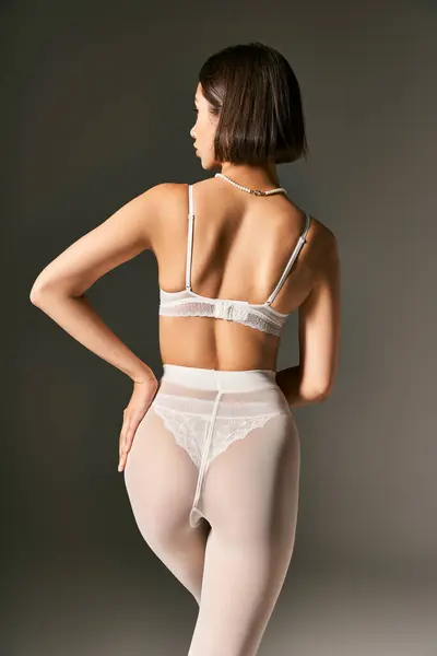 Vue arrière de la jeune femme en sous-vêtements blancs et collants posant avec la main sur la hanche sur fond gris — Photo de stock