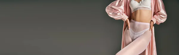 Обрізана жінка в рожевому халаті і білі колготки позує руками на стегнах на сірому фоні, банер — стокове фото