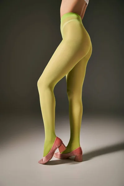 Обрезанный снимок молодой женщины в зеленых колготках, позирующей в розовых туфлях на сером фоне, чулки — стоковое фото