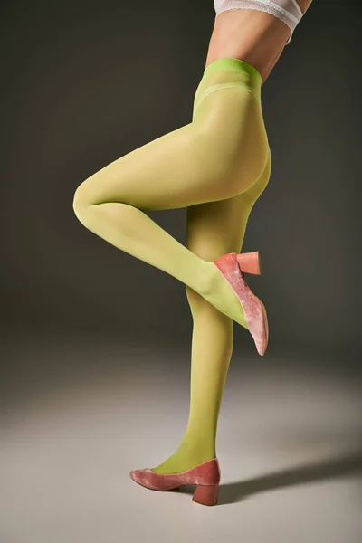 Обрезанный вид молодой женщины в зеленых колготках позируя в розовых туфлях на сером фоне, чулки — стоковое фото