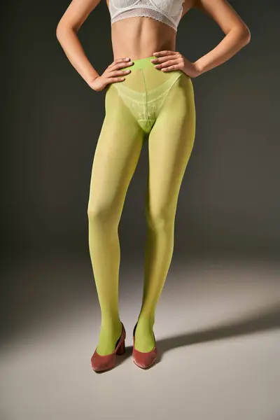 Cropped young woman in green tights and bra posing in pink shoes on grey background, hand on hips — Stock Photo