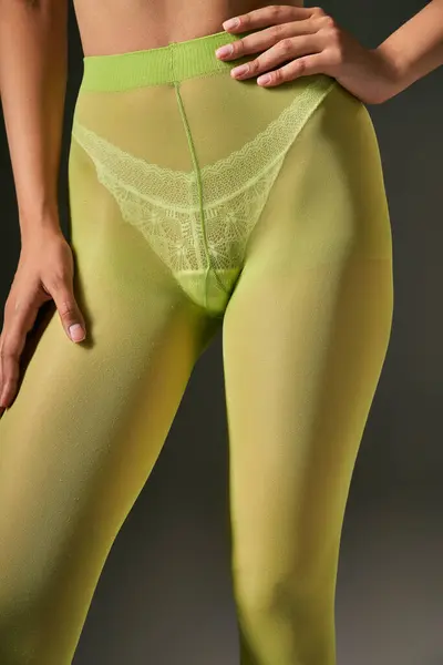Mujer joven recortada en medias verdes posando con la mano en la cadera sobre fondo gris, concepto de calcetería - foto de stock