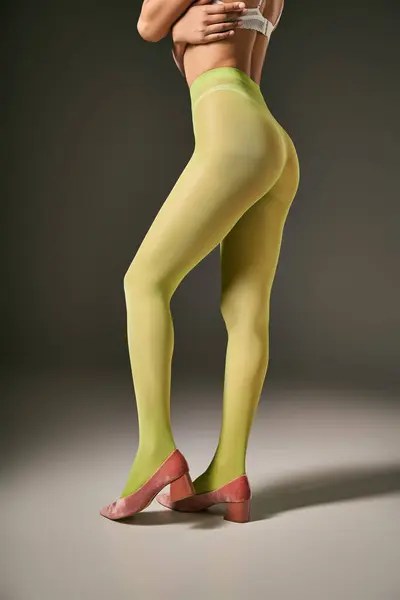 Vista recortada de mujer joven en medias de nylon verde y sujetador posando sobre fondo gris, concepto de calcetería - foto de stock