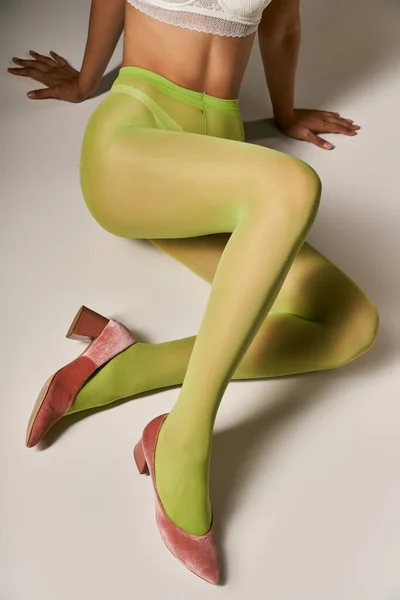 Vista recortada de la mujer en medias de nylon verde y sujetador sentado sobre fondo gris, concepto de calcetería - foto de stock