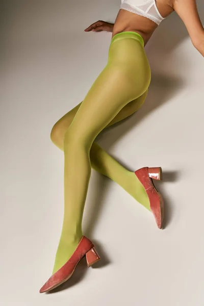 Vista recortada de la mujer en medias de nylon verde y sujetador acostado sobre fondo gris, concepto de calcetería - foto de stock