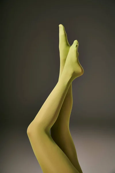 Обрезанный вид молодой женщины в зеленых нейлоновых колготках на темно-сером фоне, концепция чулочно-носочных изделий — стоковое фото