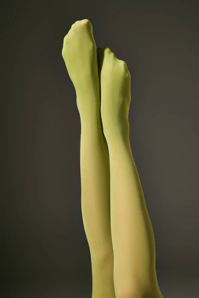 Cropped view of young woman in green nylon tights on dark grey background, raised legs — Stock Photo