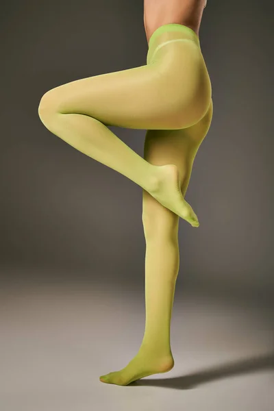 Обрезанный вид молодой женщины в зеленых нейлоновых колготках позирует на темно-сером фоне, кончик пальца ноги — стоковое фото