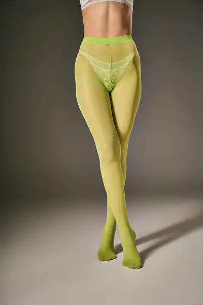 Обрезанный вид молодой женщины в зеленых нейлоновых колготках позирует на темно-сером фоне, скрещенные ноги — стоковое фото