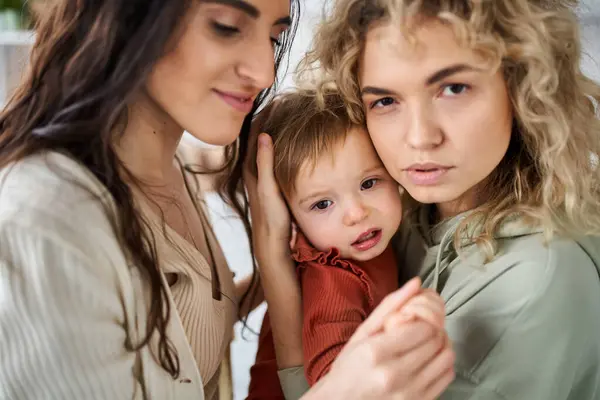 Beautiful loving lesbian couple holding their baby girl in hands and comforting her, family concept — Stock Photo