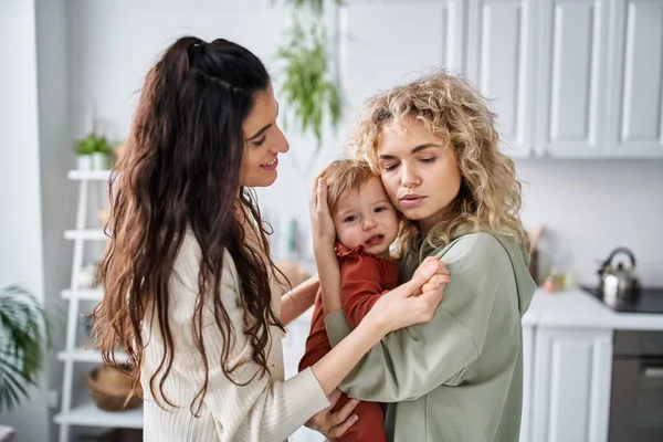 Beautiful caring lesbian couple holding their baby girl in hands and comforting her, family concept — Stock Photo