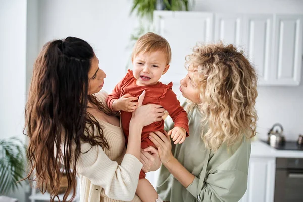 Loving lgbt couple in homewear holding their baby girl in hands and comforting her, family concept — Stock Photo