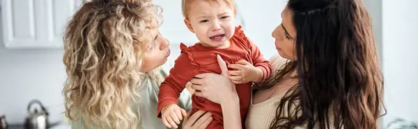 Caring lgbt couple in homewear holding their baby girl in hands and comforting her, family concept — Stock Photo