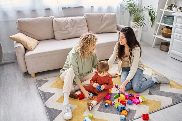 Joyeux couple lesbien aimant jouer avec des jouets avec leur fille tout-petit à la maison, parentalité moderne — Photo de stock