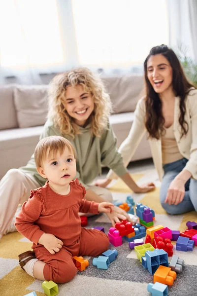 Alegre pareja lesbiana jugando con juguetes con su hija pequeña en casa, crianza moderna - foto de stock