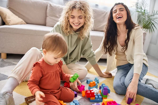 Alegre hermosa pareja de lesbianas jugando con su hija en casa, crianza moderna - foto de stock