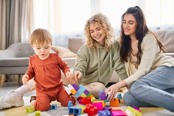 Joyous beautiful lesbian couple playing with their toddler daughter at home, modern parenting — Stock Photo