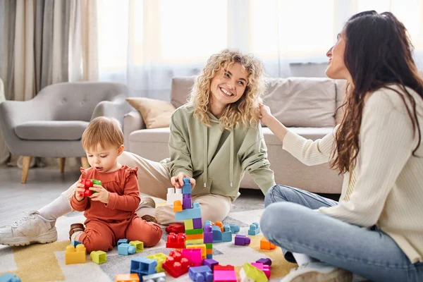 Cheerful attractive lgbt couple playing with baby girl with toys on floor at home, family concept — Stock Photo