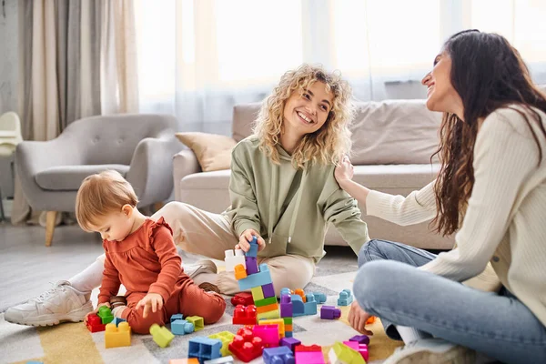 Joyeux couple attentionné lgbt jouer avec leur petite fille avec des jouets sur le sol à la maison, concept de famille — Photo de stock
