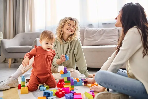 Delighted lesbian couple playing with their baby girl with toys on floor at home, family concept — Stock Photo