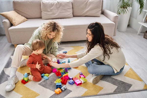 Fröhliches lesbisches Paar spielt mit ihrem kleinen Mädchen mit Spielzeug auf dem Boden zu Hause, Familienkonzept — Stockfoto