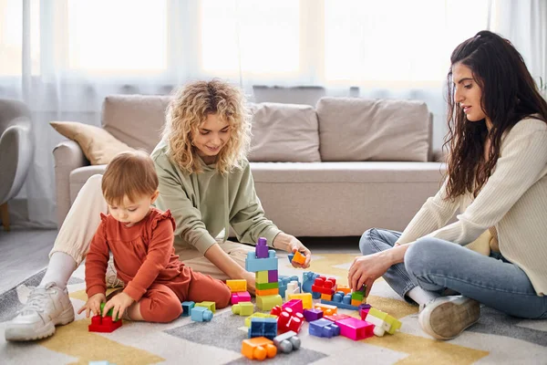 Alegre atractiva pareja lesbiana jugando con su hija pequeña en casa, crianza moderna - foto de stock
