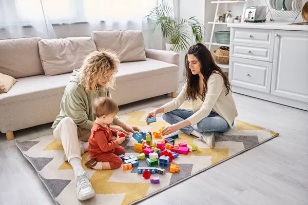 Cheerful loving lesbian couple playing with their toddler daughter at home, modern parenting — Stock Photo