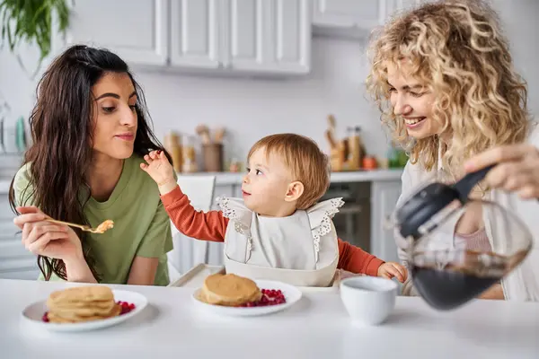 Joyful beautiful lgbt couple having delicious breakfast with their baby girl, family concept — Stock Photo