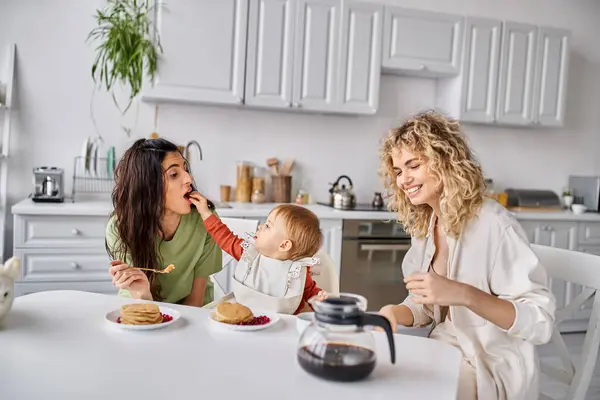 Joyeux couple lgbt attrayant avoir délicieux petit déjeuner avec leur petite fille, concept de famille — Photo de stock