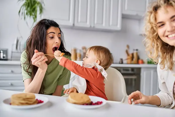 Affectionate lesbian couple having breakfast with their small pretty daughter, family concept — Stock Photo
