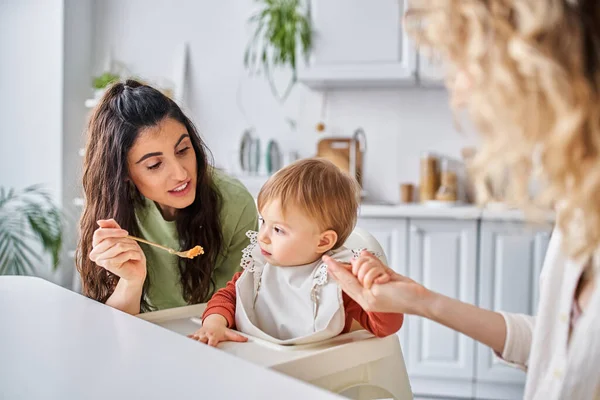 Centrarse en la alegre morena mujer con hija pequeña desayunando al lado de la pareja borrosa, familia - foto de stock