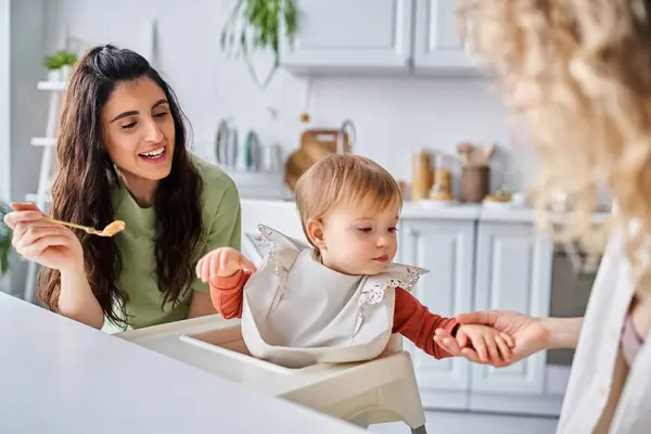 Focus on happy brunette woman with small daughter having breakfast next to blurred partner, family — Stock Photo