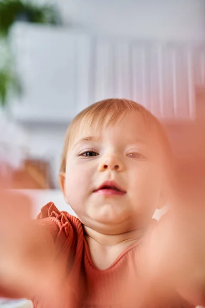 Nahaufnahme von niedlichen charmanten Baby-Mädchen in orangefarbenem Pullover versucht, die Kamera mit ihren Händen zu erreichen — Stockfoto